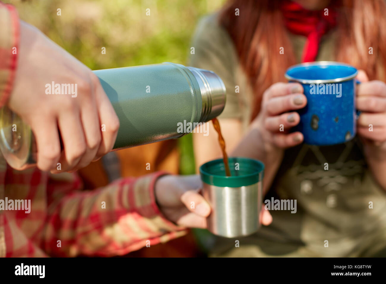 Two women sharing a thermal flask of coffee outdoors in nature as they take a rest from a day of hiking Stock Photo -
