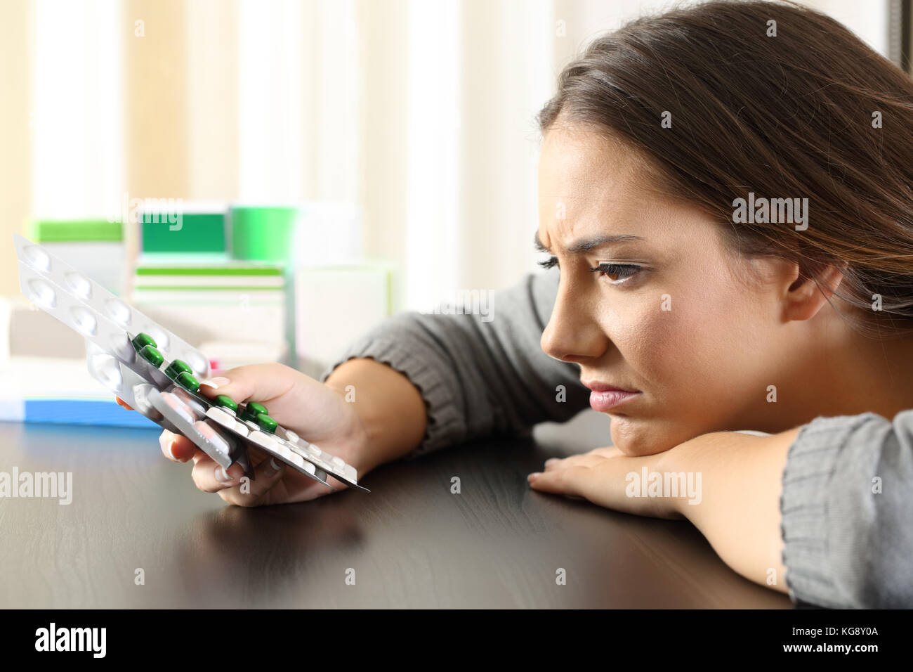 Side view portrait of a doubtful woman holding a lot of medicines on a table at home Stock Photo