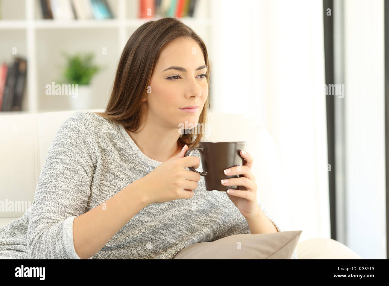 Portrait of a pensive girl holding a cup of coffee sitting on a sofa at home Stock Photo