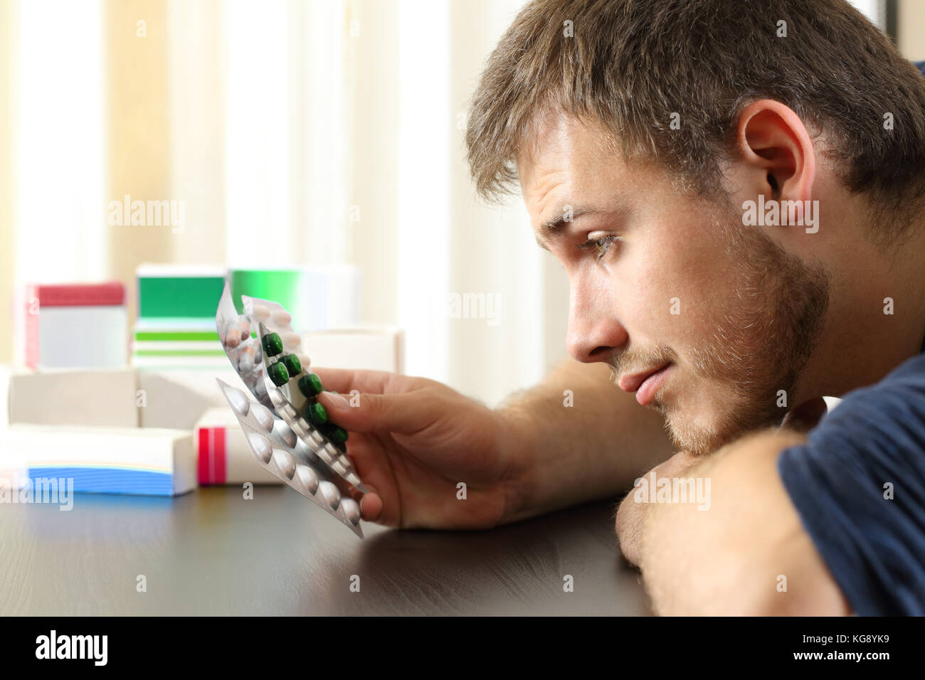 Side view portrait of a doubtful man holding a lot of medicines sitting at home Stock Photo