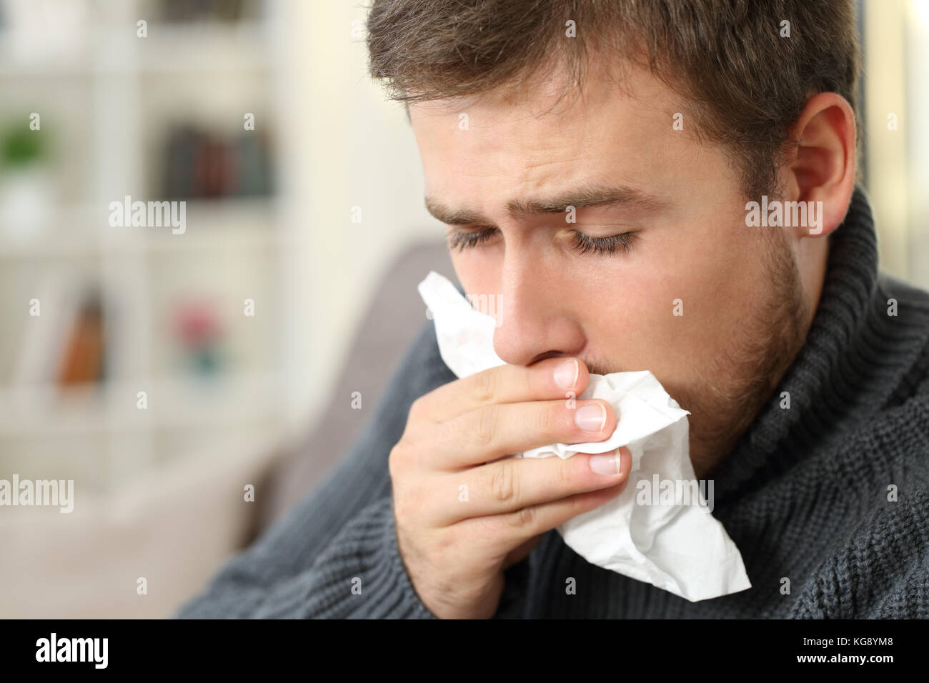 Man coughing covering mouth with a tissue sitting on a couch in a house