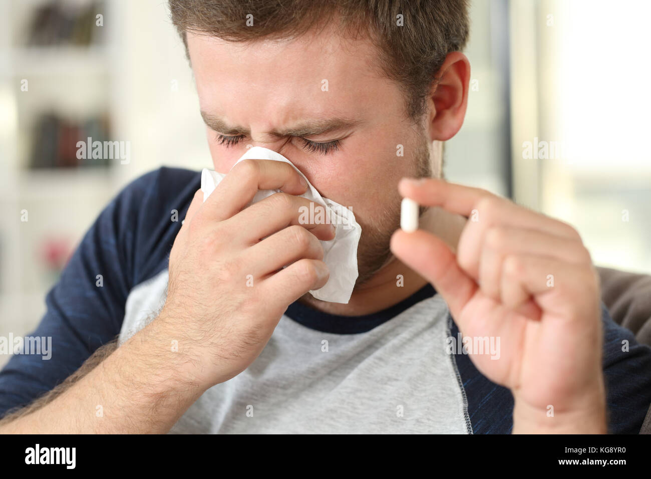 Sick man coughing using a tissue and holding a pill sitting on a sofa