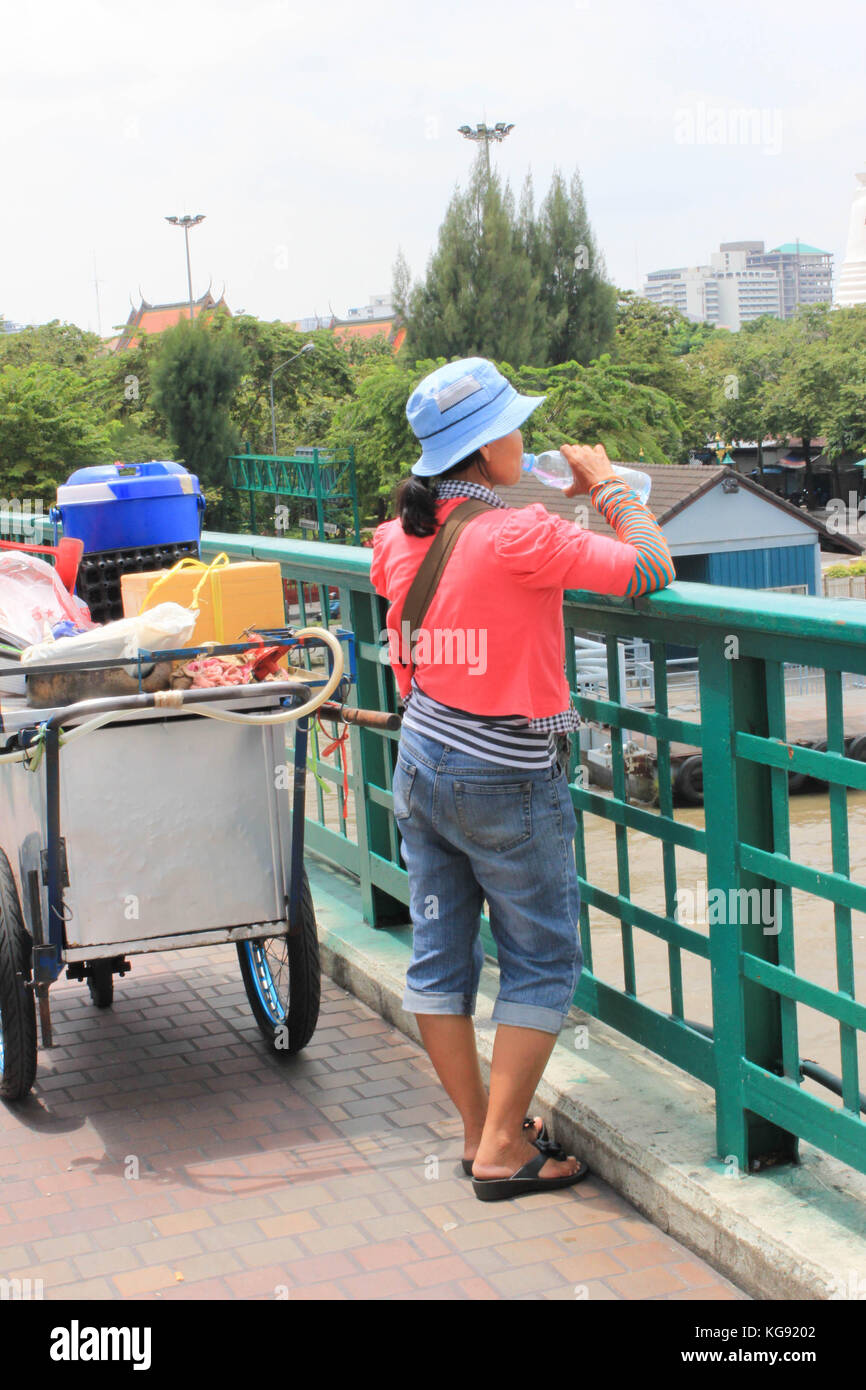 Female vendor stopping on the bridge to take a drink Stock Photo
