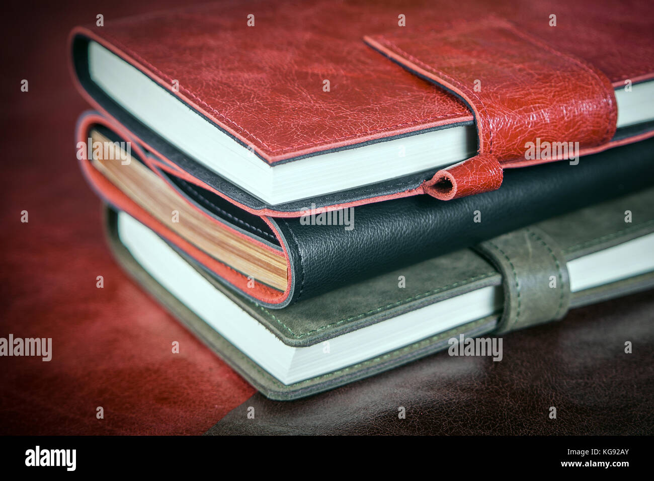 A close-up of three diaries, covered with genuine leather with a clasp: gray, red and black. Leather hand-made notebooks on a table in one row Stock Photo