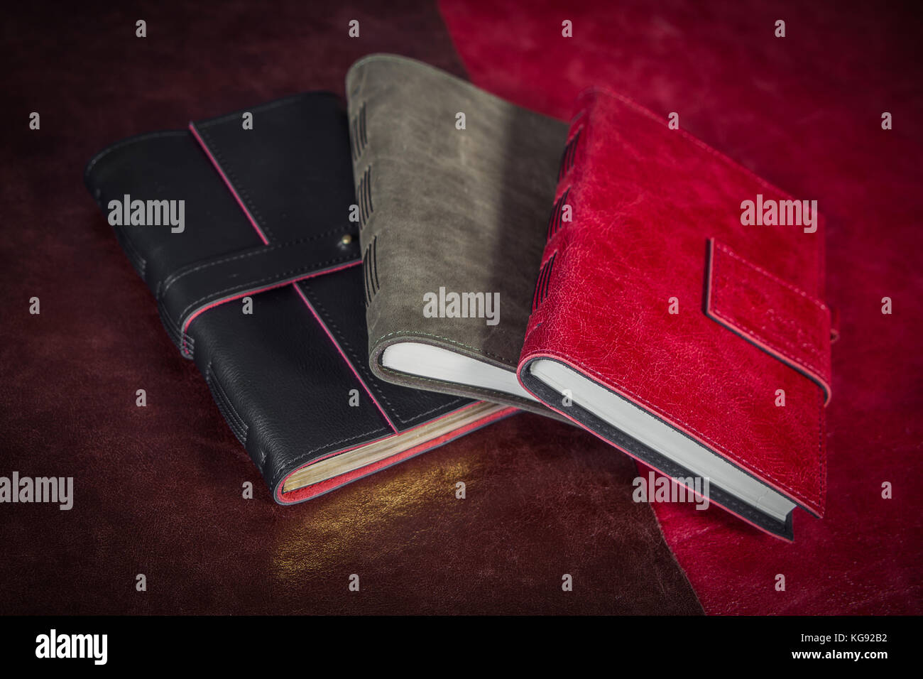 A close-up of three diaries, covered with genuine leather with a clasp: gray, red and black. Leather hand-made notebooks on a  table Stock Photo