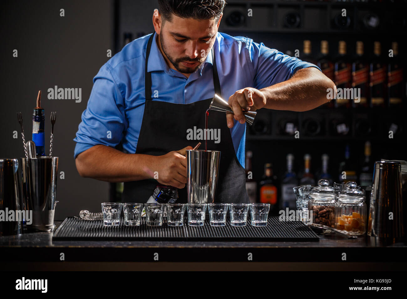 Bartender with jigger pouring syrup into shaker and preparing cocktail