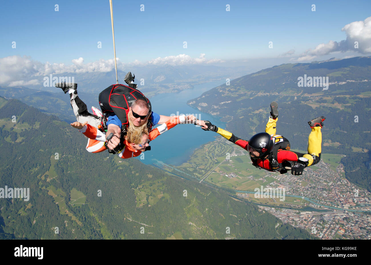 Tandem skydiving jump over a beautiful mountain area, together with a fun jumper holding hands. Can you see their smiley faces? Stock Photo