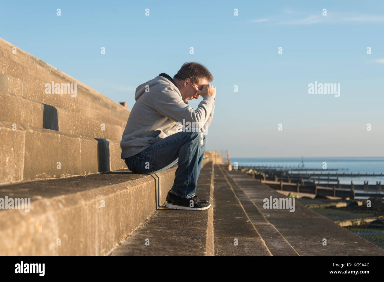 man with his head in his hands sitting on steps outside by the sea Stock Photo