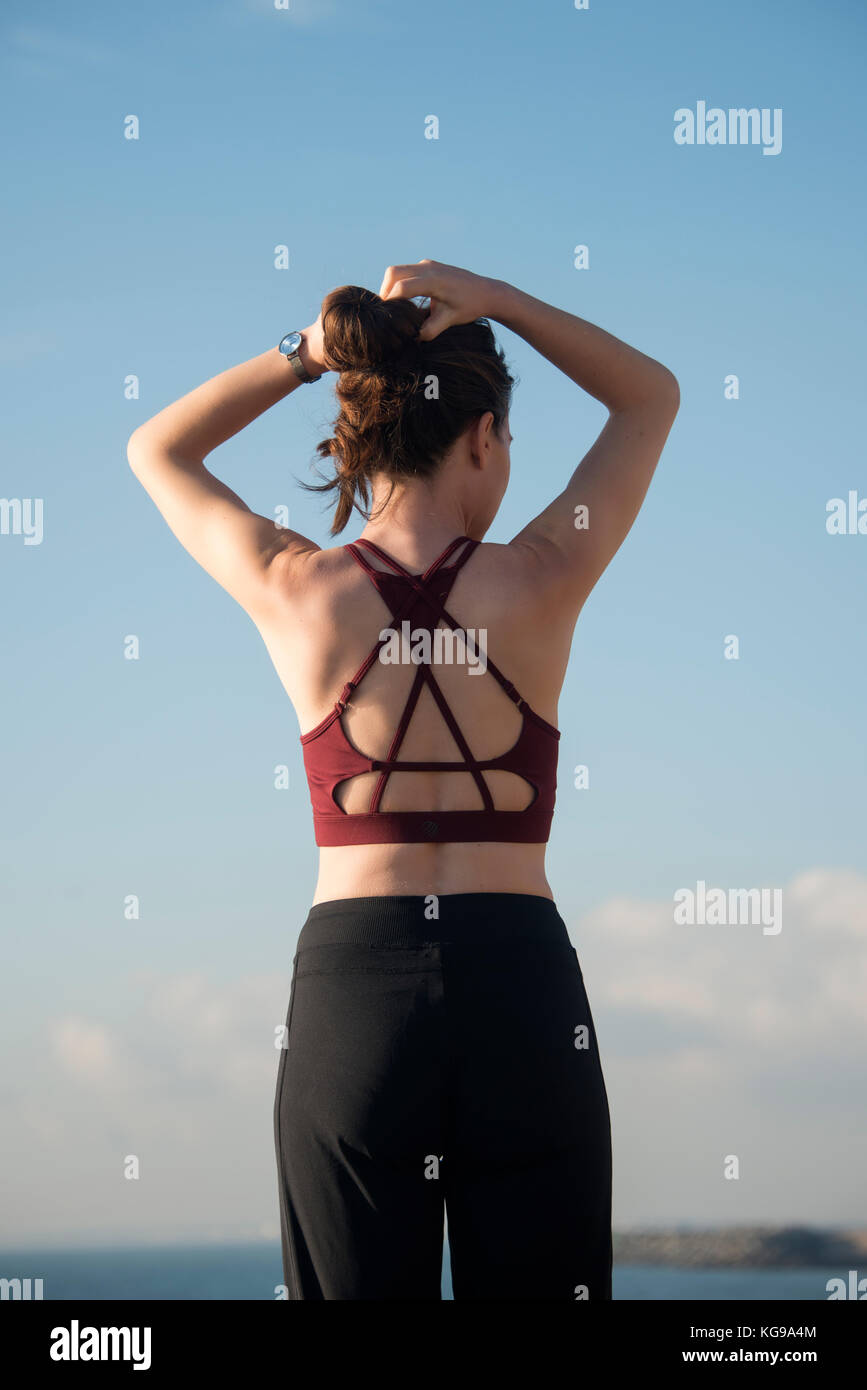 sporty woman tying her hair up before starting exercise and training wearing a sports bra, back view. Stock Photo