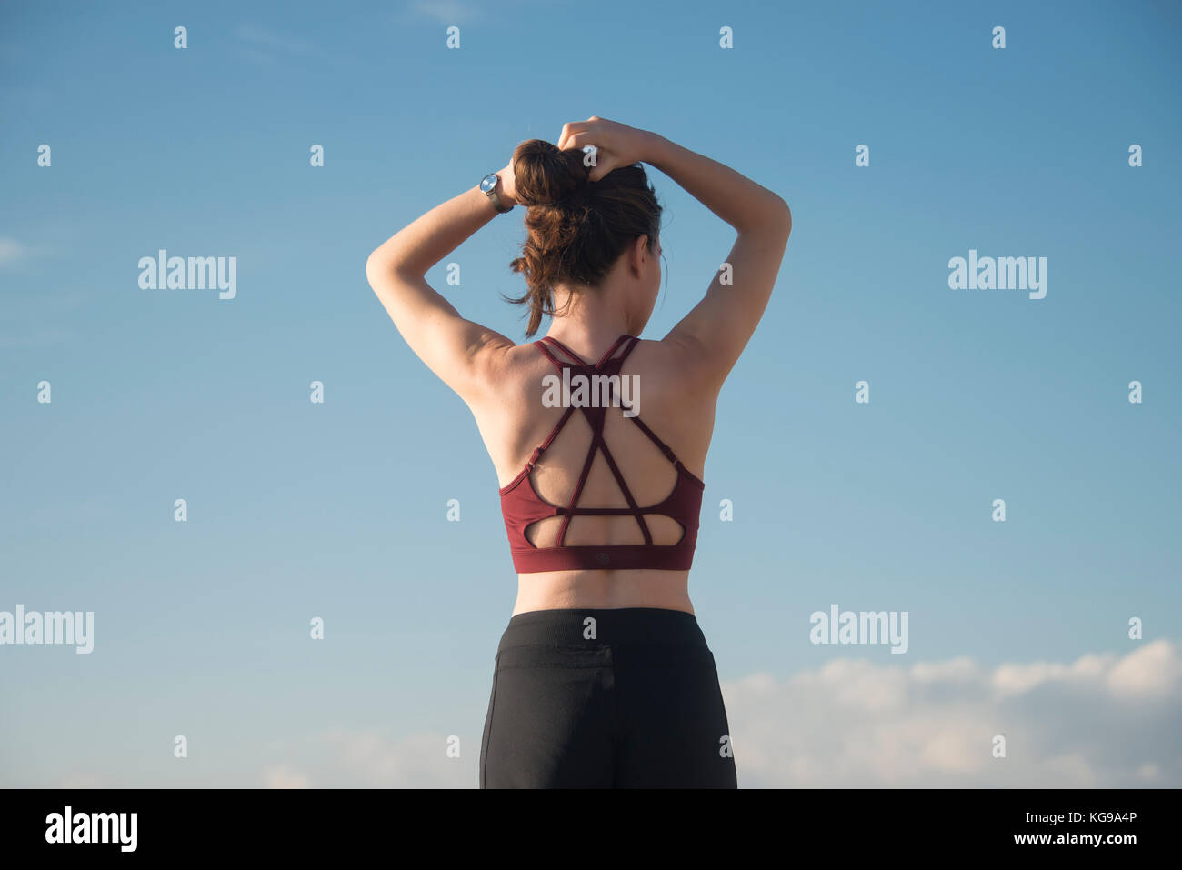 sporty woman tying her hair up before starting exercise and training wearing a sports bra, back view. Stock Photo