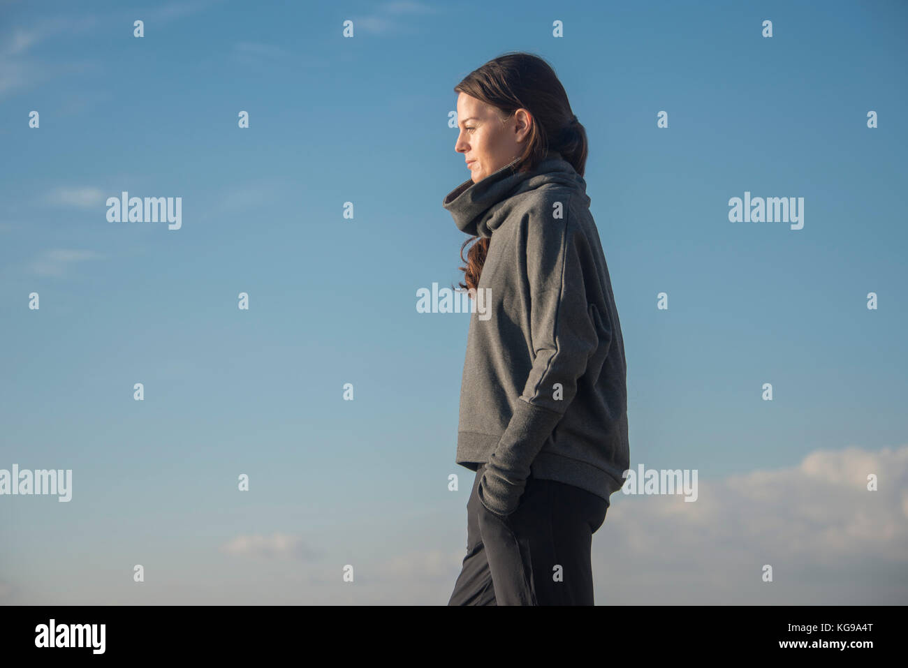 Woman standing with hands in pockets looking out to sea Stock Photo