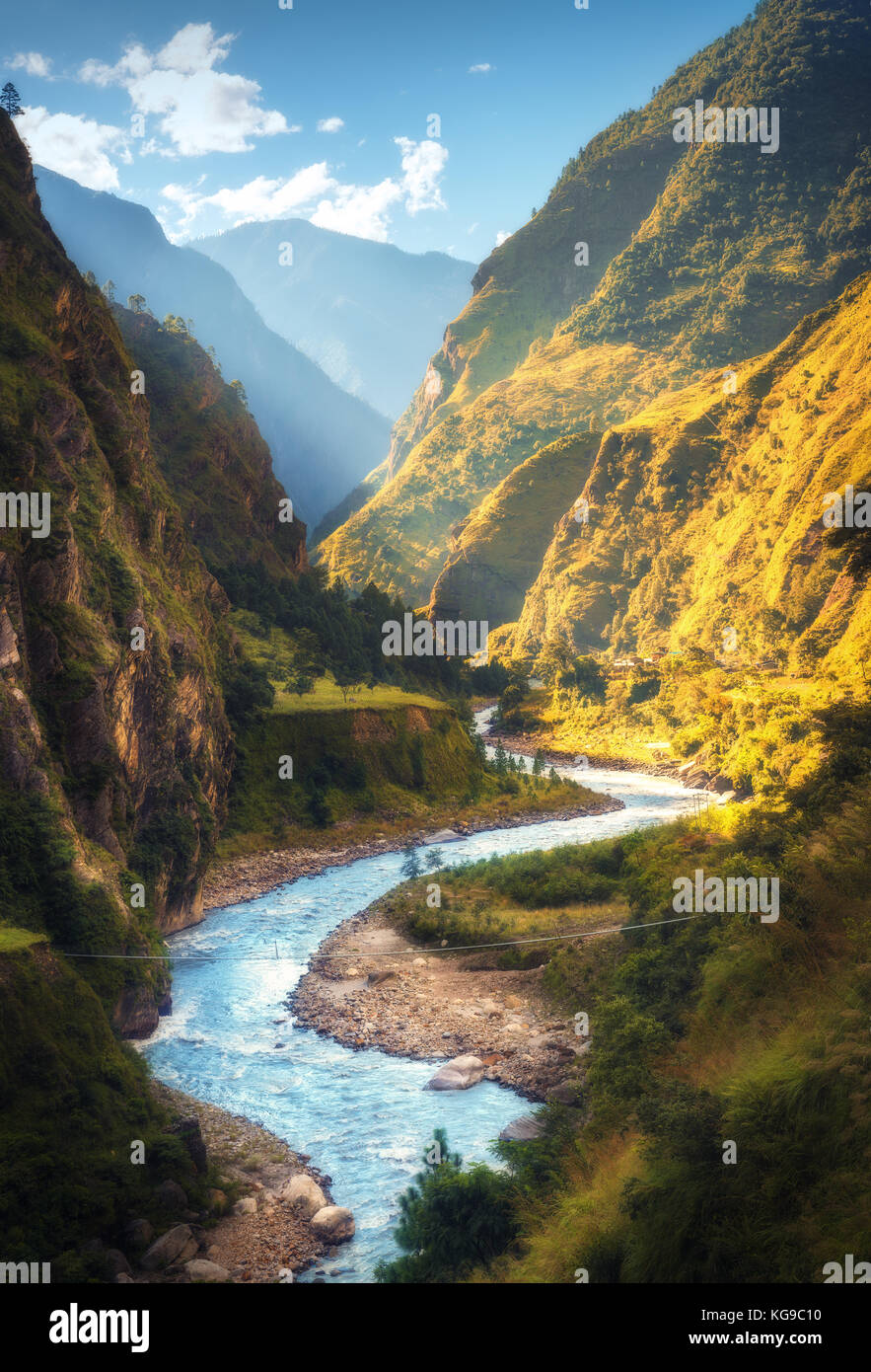 Amazing landscape with high Himalayan mountains, beautiful curving river, green forest, blue sky with clouds and yellow sunlight in autumn in Nepal. M Stock Photo
