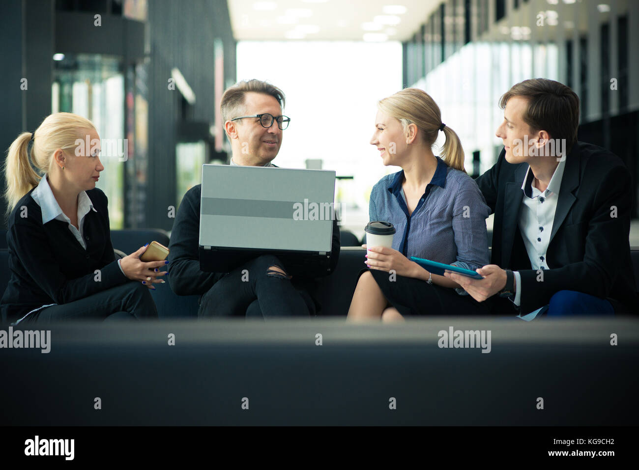 Business team sitting in office lobby with laptop and talking Stock ...