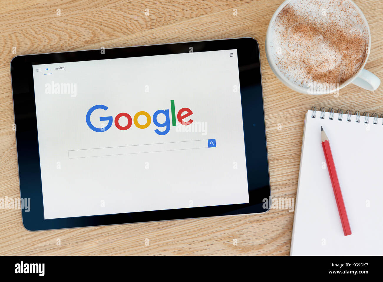 The Google website features on an iPad tablet device which rests on a wooden table beside a notepad and pencil and a cup of coffee (Editorial use only Stock Photo
