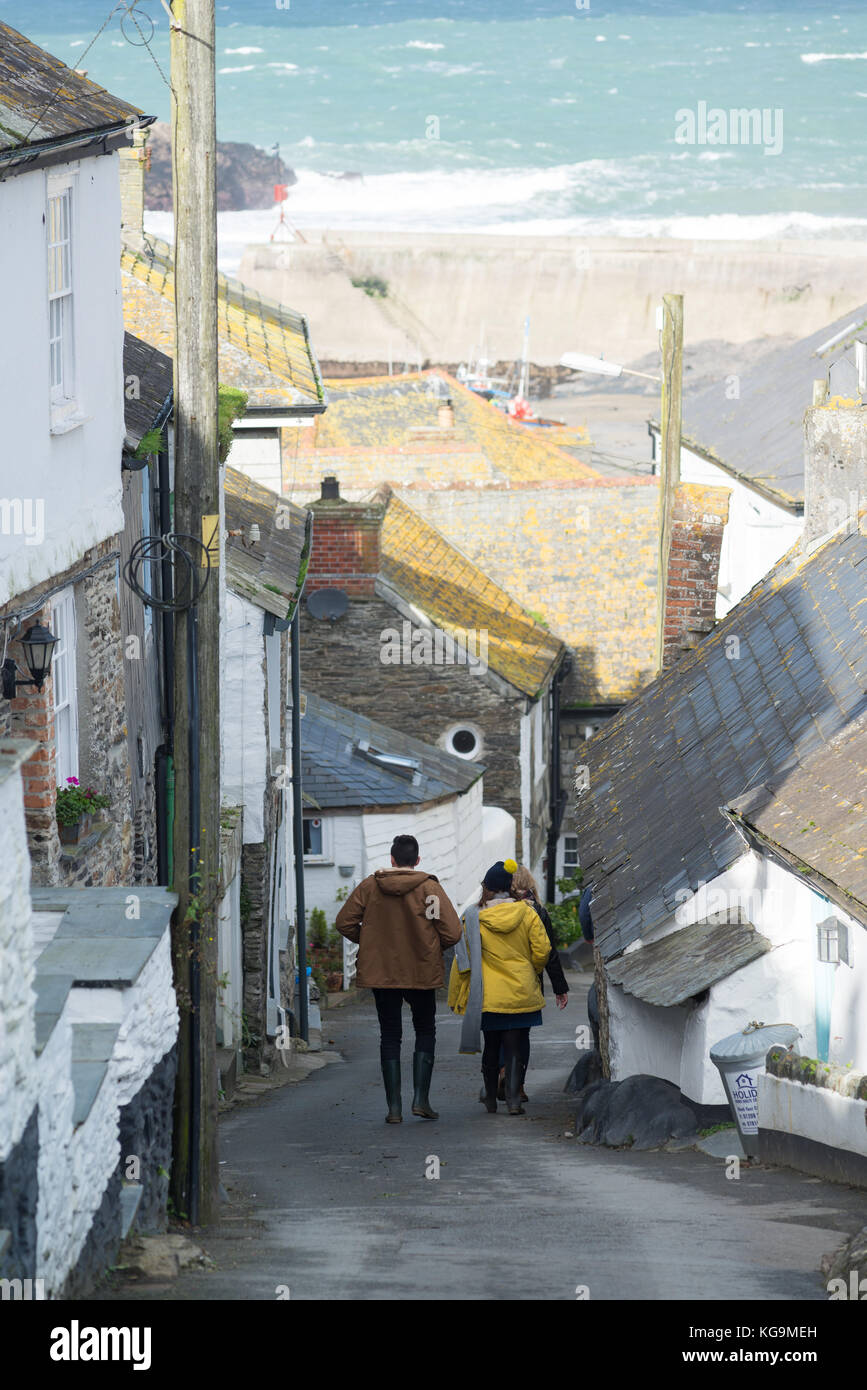 People walking down a steep hill towards the harbour, Port Isaac, Cornwall, UK, November. Stock Photo