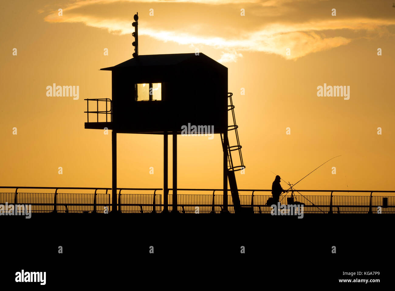A fisherman looks on as the sun rises over Cardiff Bay barrage in Cardiff, Wales. Forecasters have predicted a week-long chill which has been put down Stock Photo