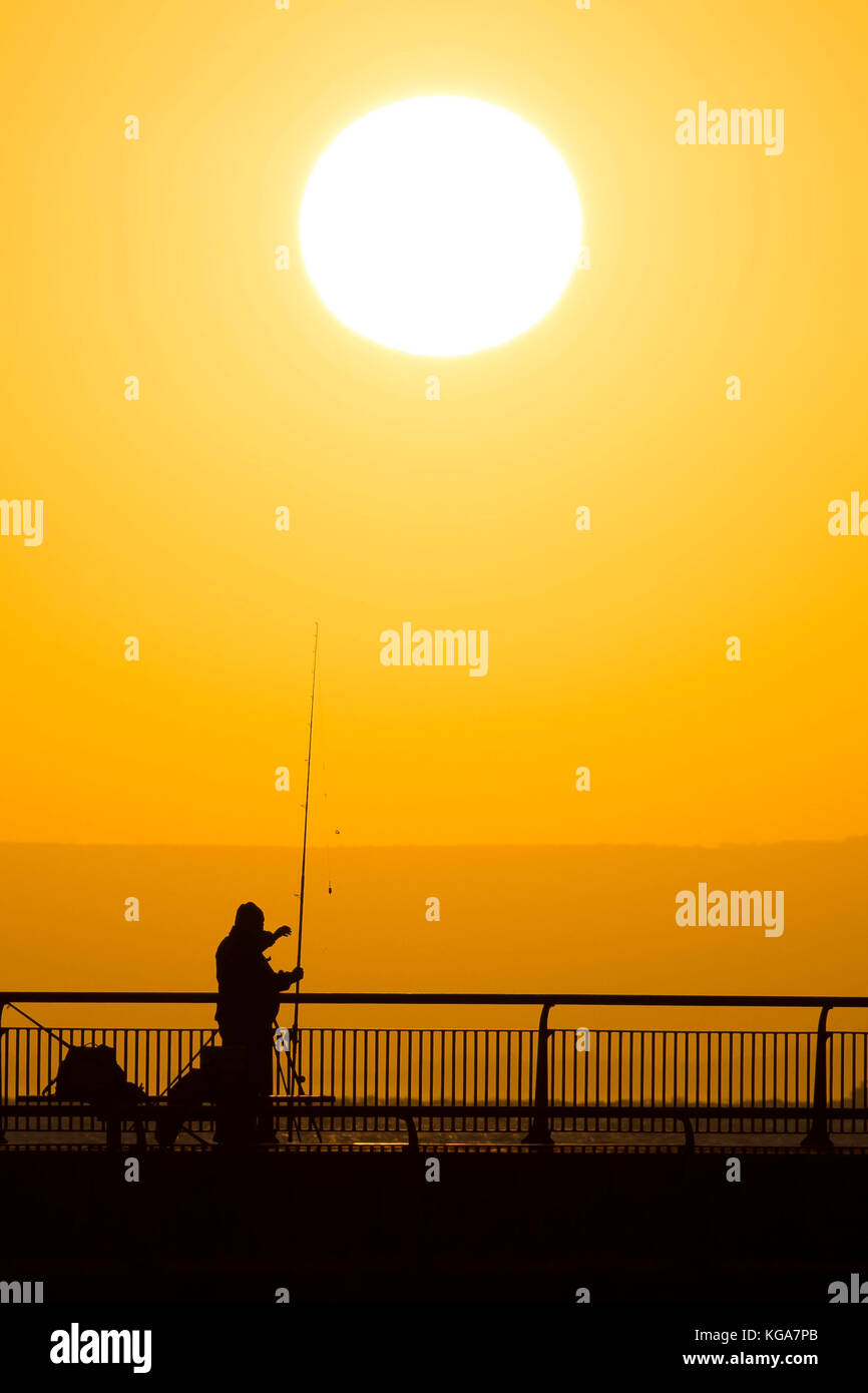 A fisherman looks on as the sun rises over Cardiff Bay barrage in Cardiff, Wales. Forecasters have predicted a week-long chill which has been put down Stock Photo