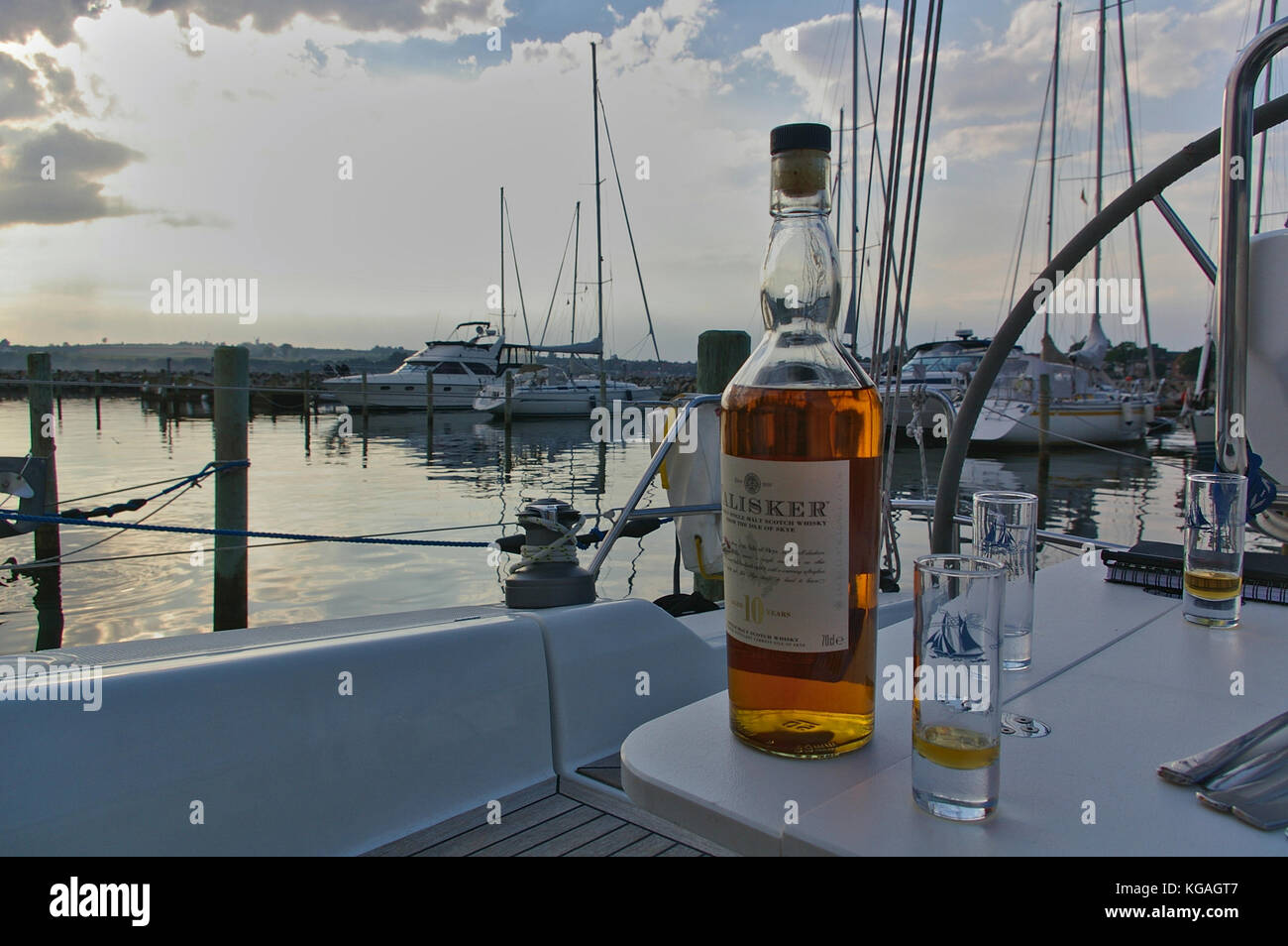 Sonderborg, Denmark - June 30th, 2012 - Bottle of single malt whisky with glasses on the table in the cockpit of a sailing yacht with a marina in the  Stock Photo