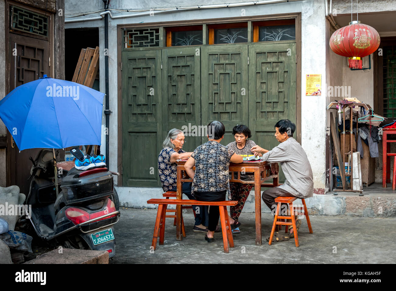Four older Chinese people play a game at a wooden table in an alley at Cangpo Ancient Village, Yongjia County, Zhejiang Province, China, village life Stock Photo