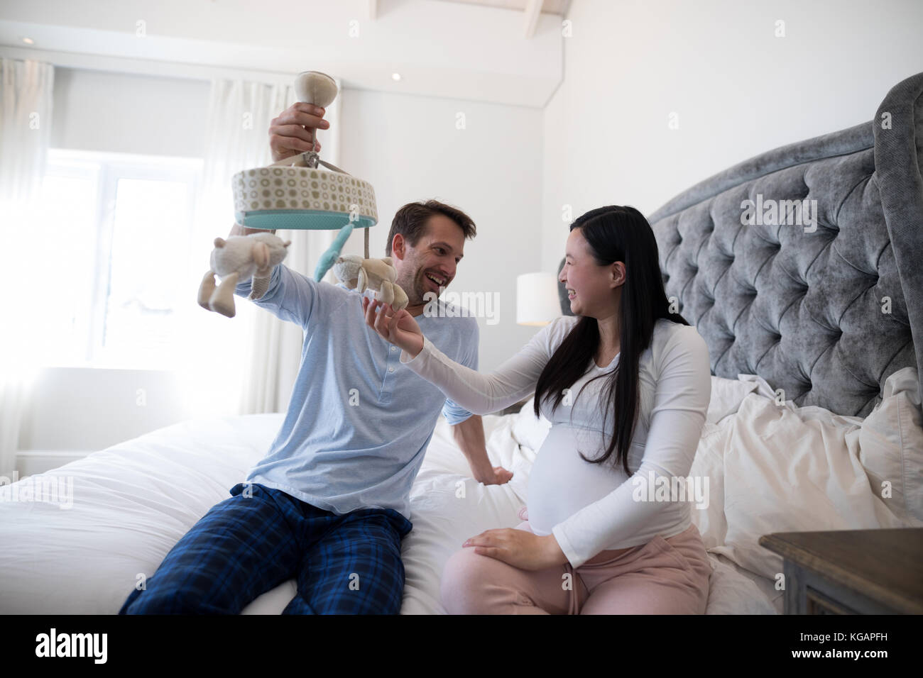 Happy man and pregnant woman holding toy in bedroom Stock Photo