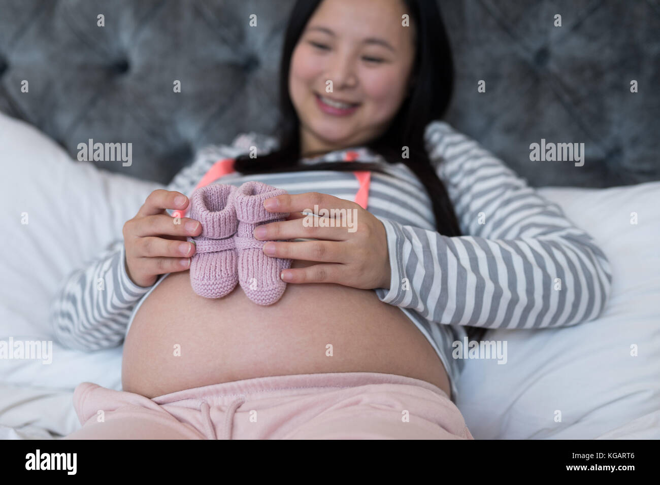 Pregnant woman looking at socks in bedroom Stock Photo