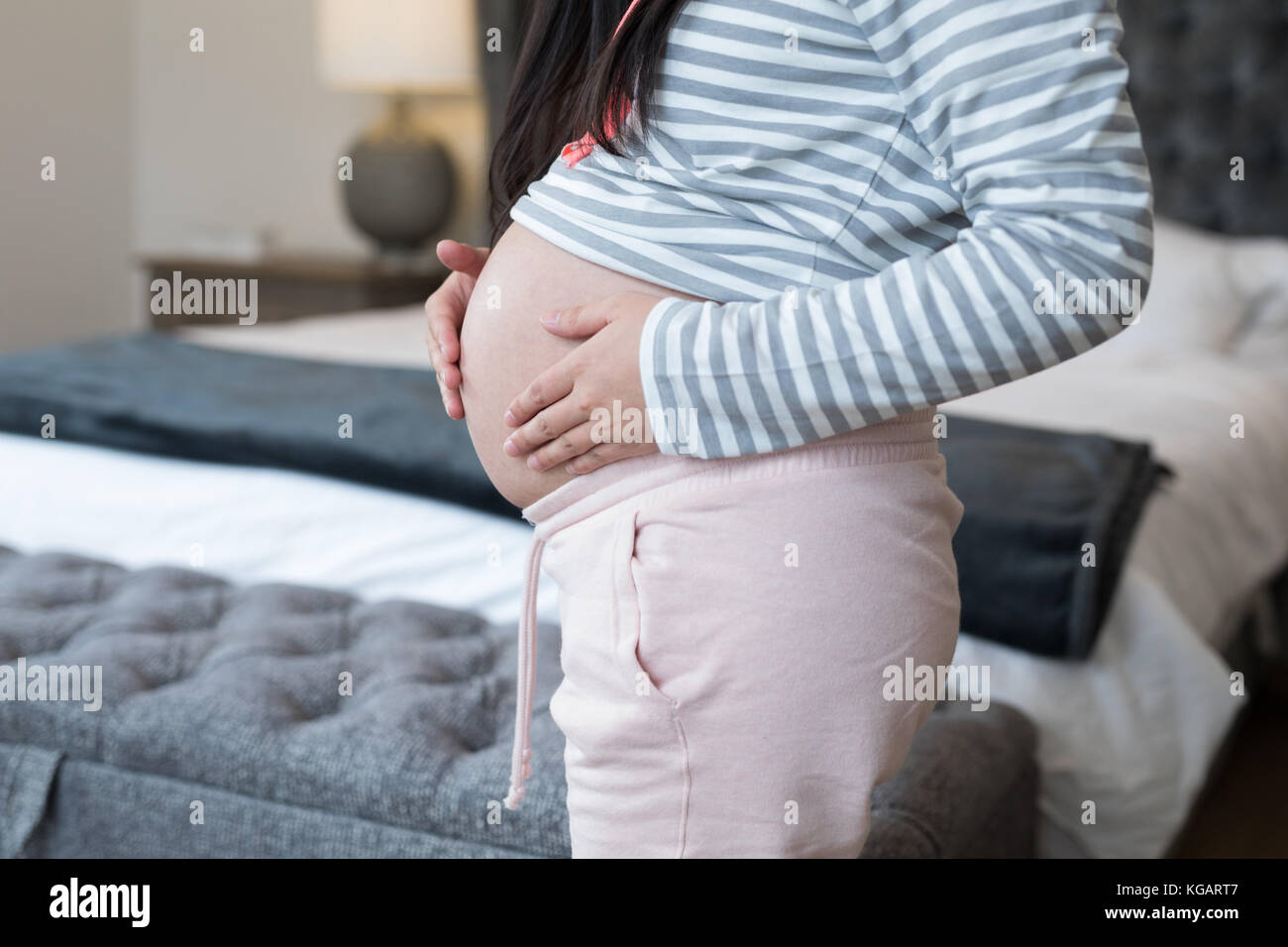 Mid section of pregnant woman touching her stomach in bedroom Stock Photo
