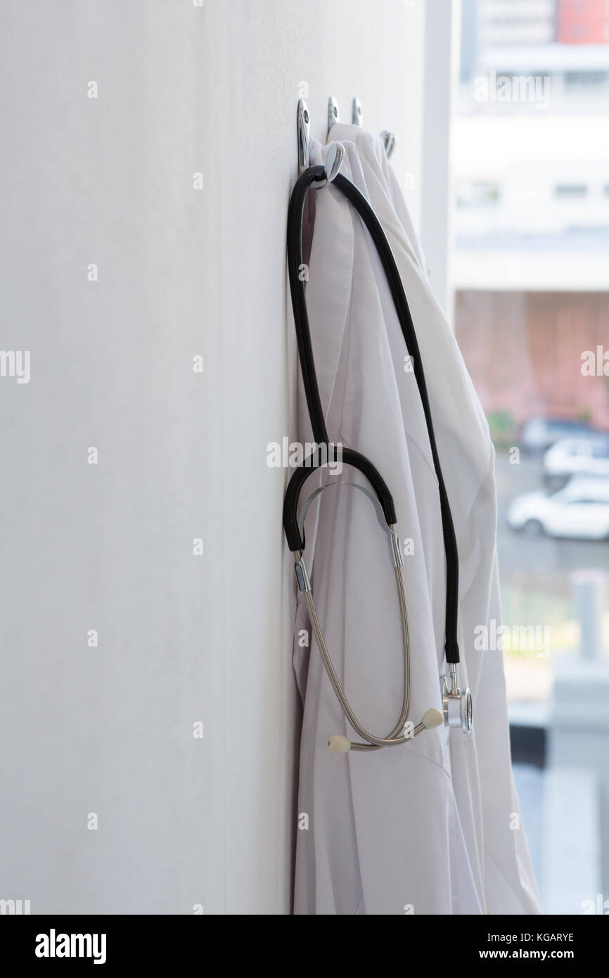Laboratory coat and stethoscope hanging on hook against wall Stock Photo