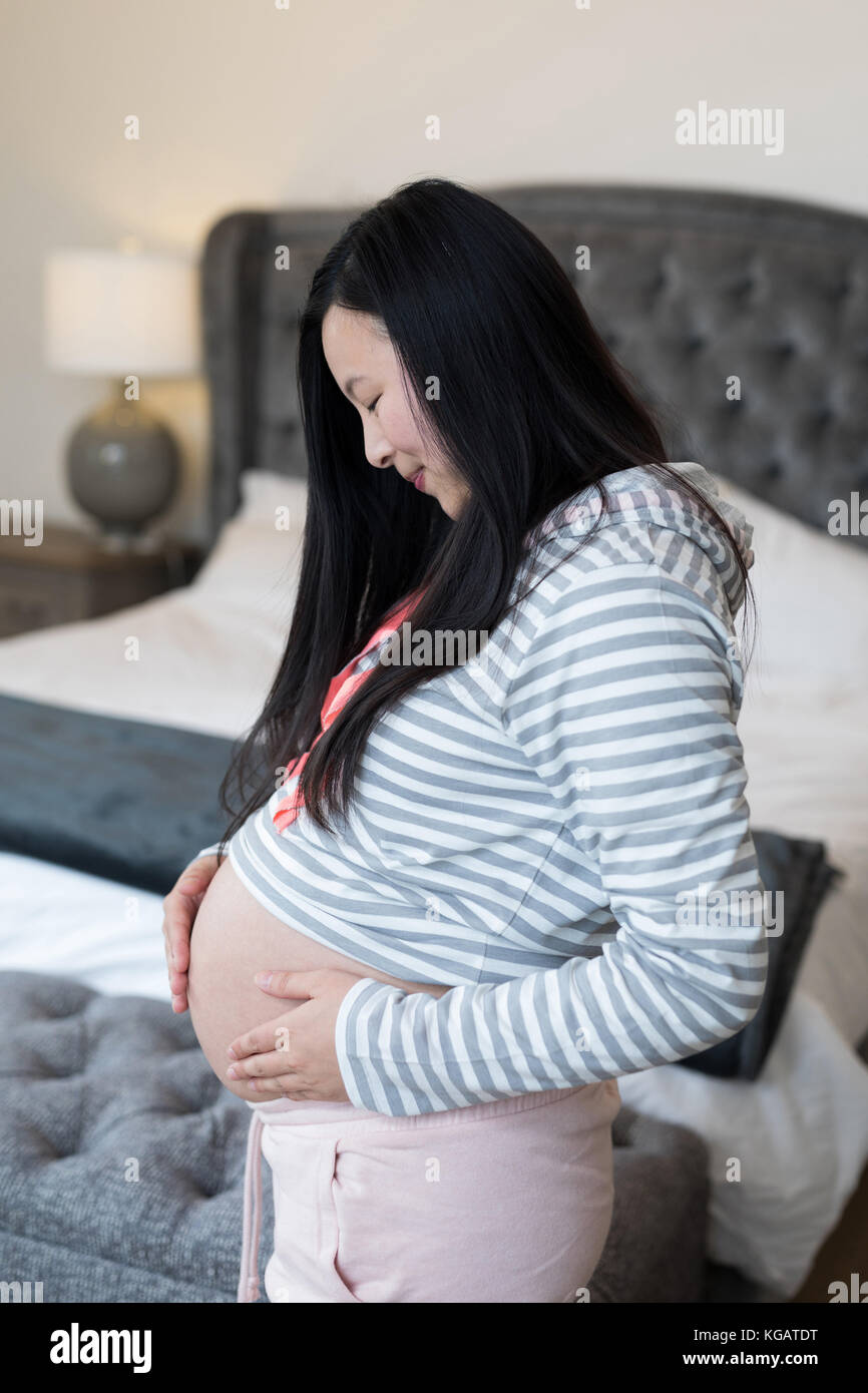 Pregnant woman touching her stomach in bedroom Stock Photo
