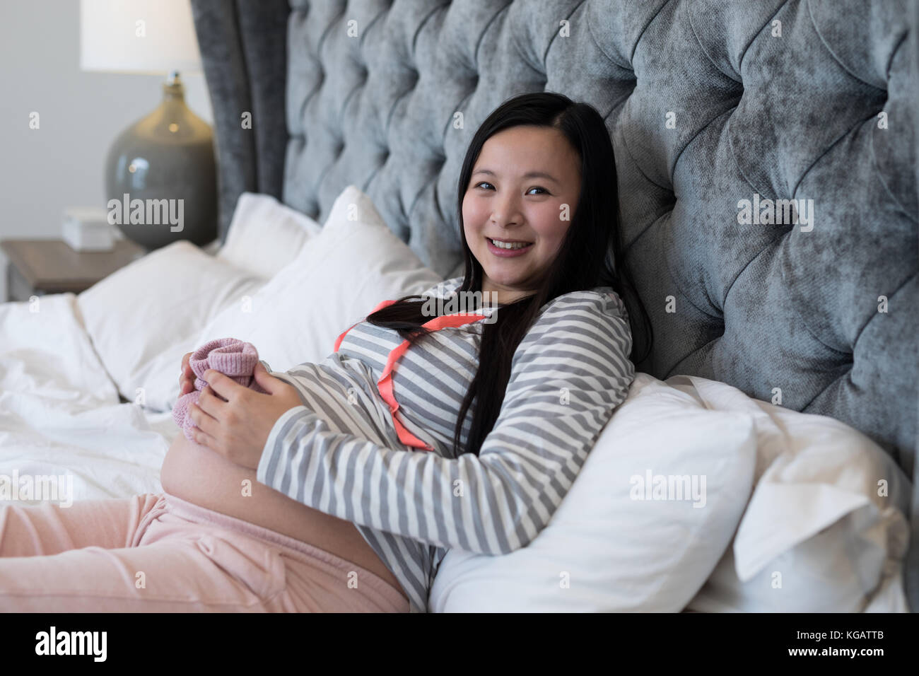 Portrait of pregnant woman looking at holding socks in bedroom Stock Photo