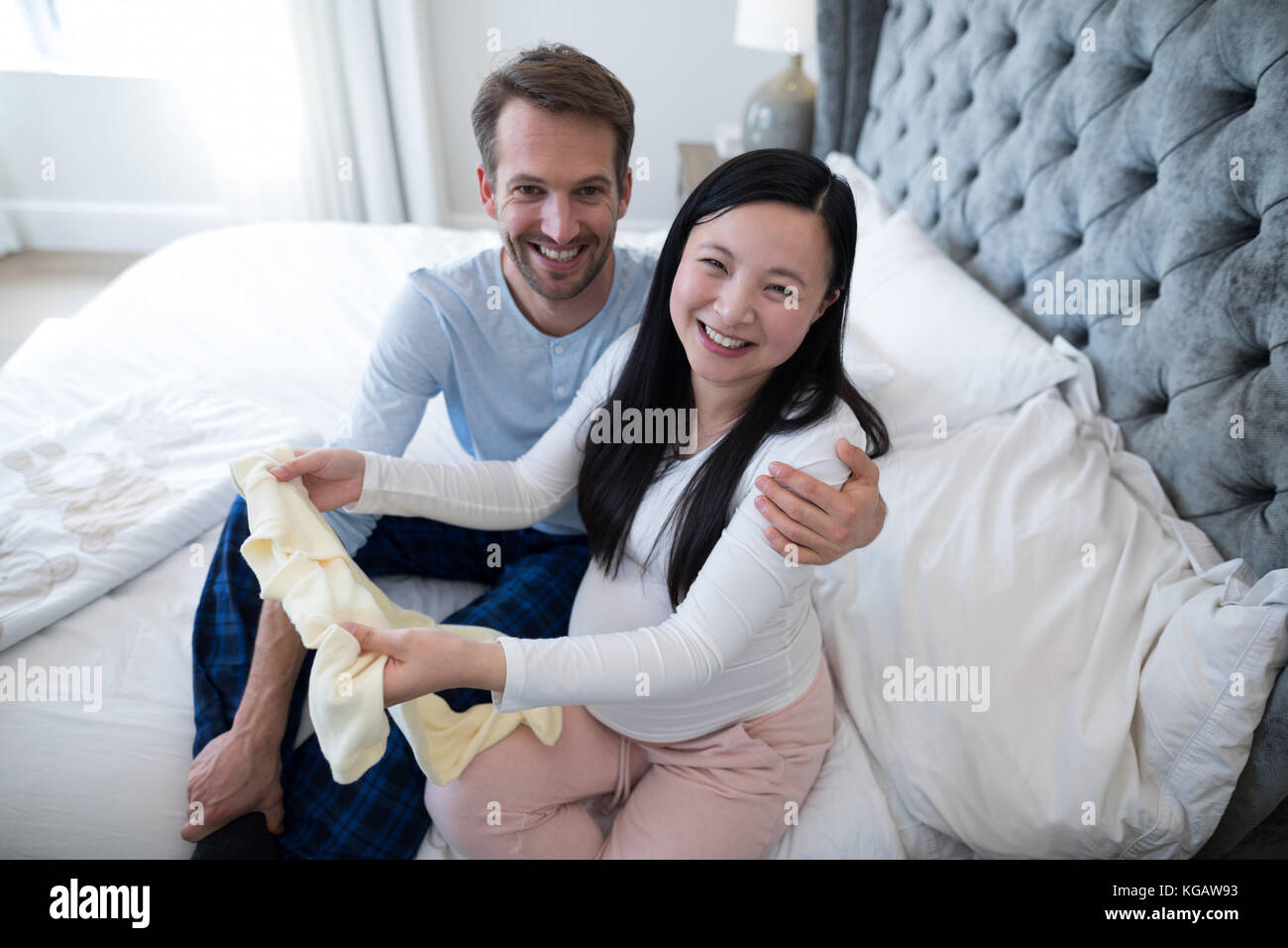 Portrait of happy couple holding baby clothes in bedroom Stock Photo