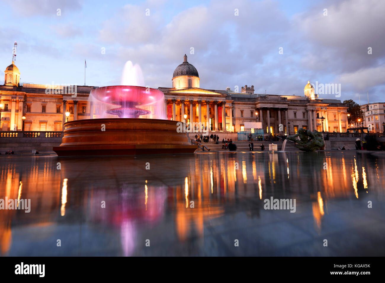 National Gallery in Trafalgar Square London with reflection in fountain water. Dusk, evening with lights, people Stock Photo