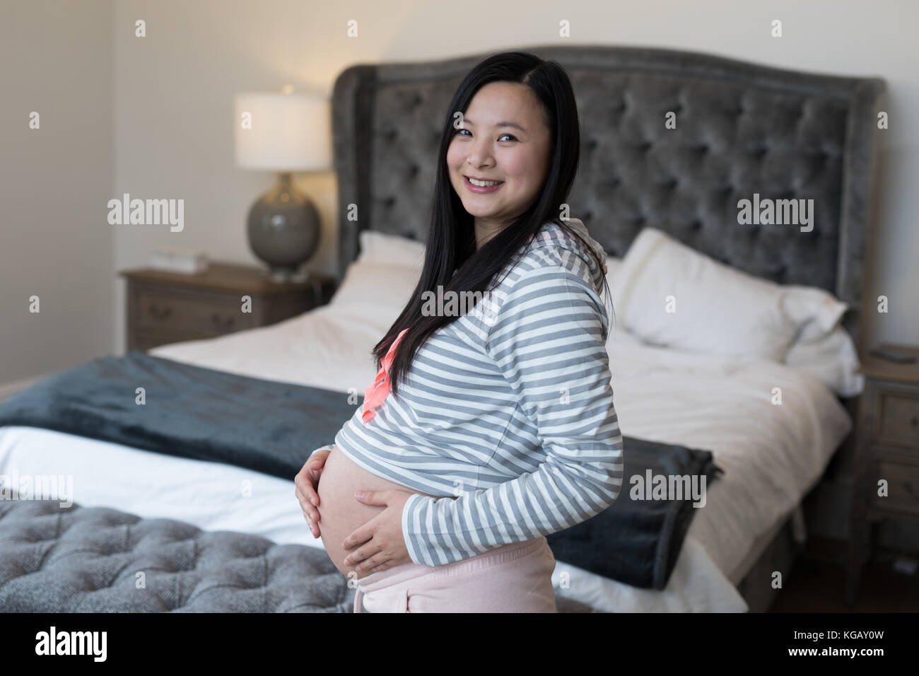 Portrait of pregnant woman touching her stomach in bedroom Stock Photo