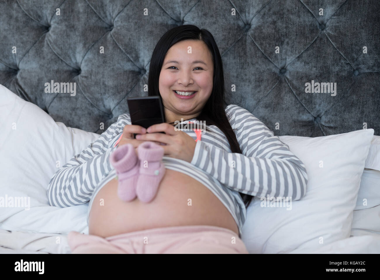 Portrait of woman using mobile with pair of socks on her stomach Stock Photo