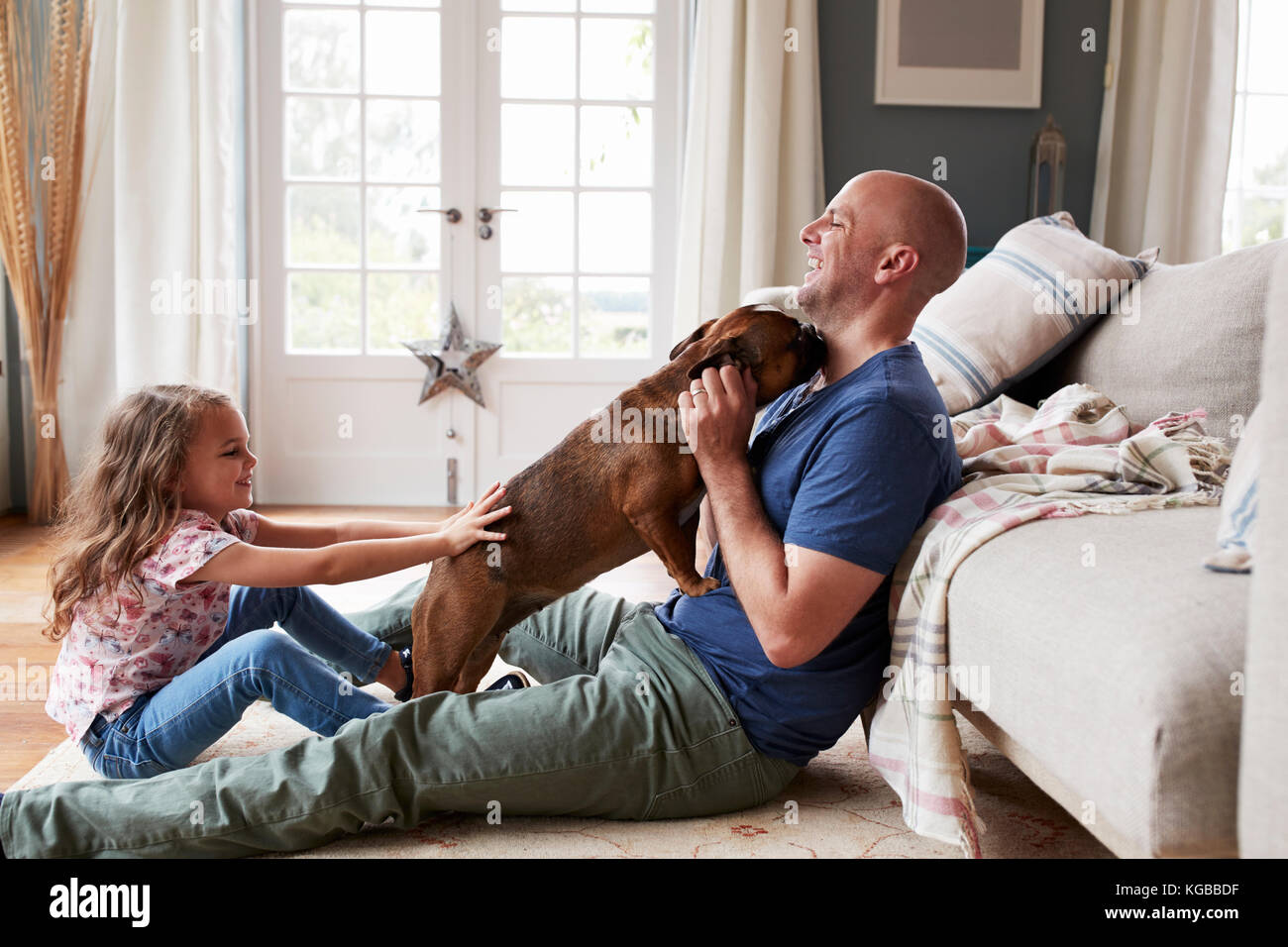 Father and daughter having fun with their pet dog at home Stock Photo