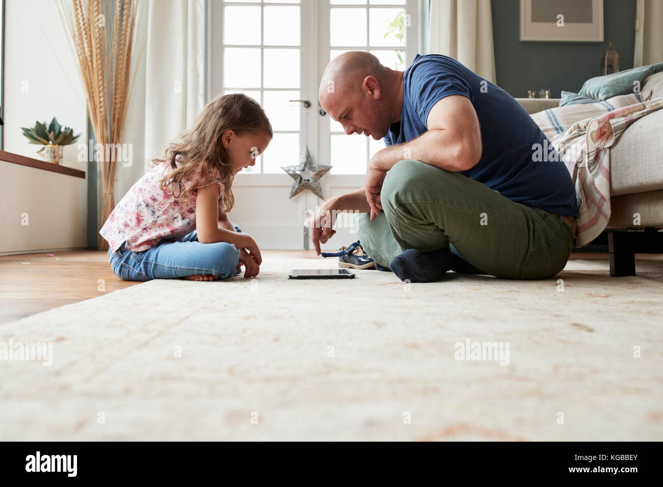 Girl and dad sit on the floor playing with tablet computer Stock Photo