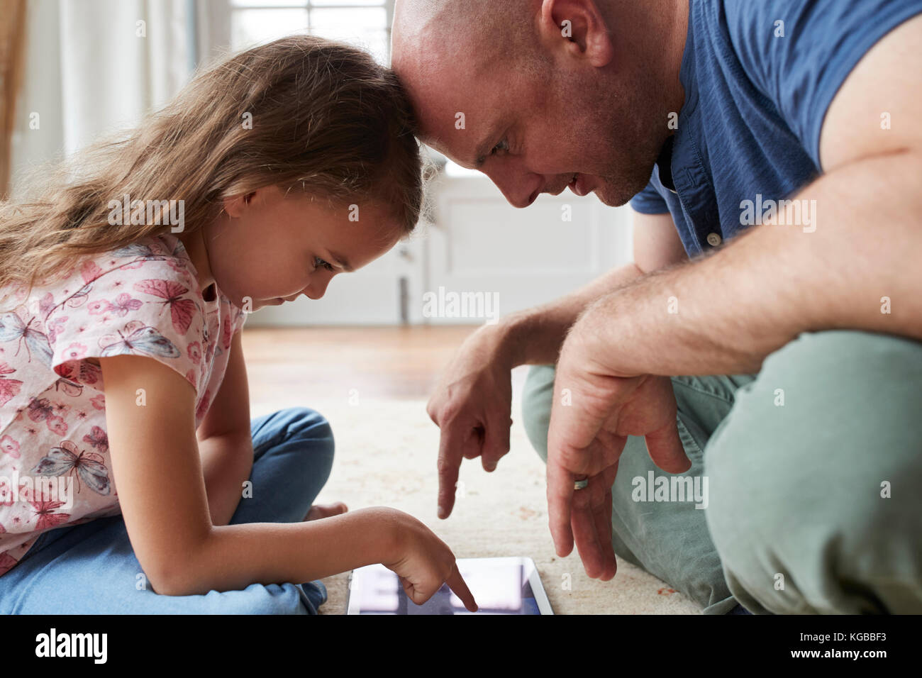 Girl and dad sit on the floor playing with tablet, close up Stock Photo
