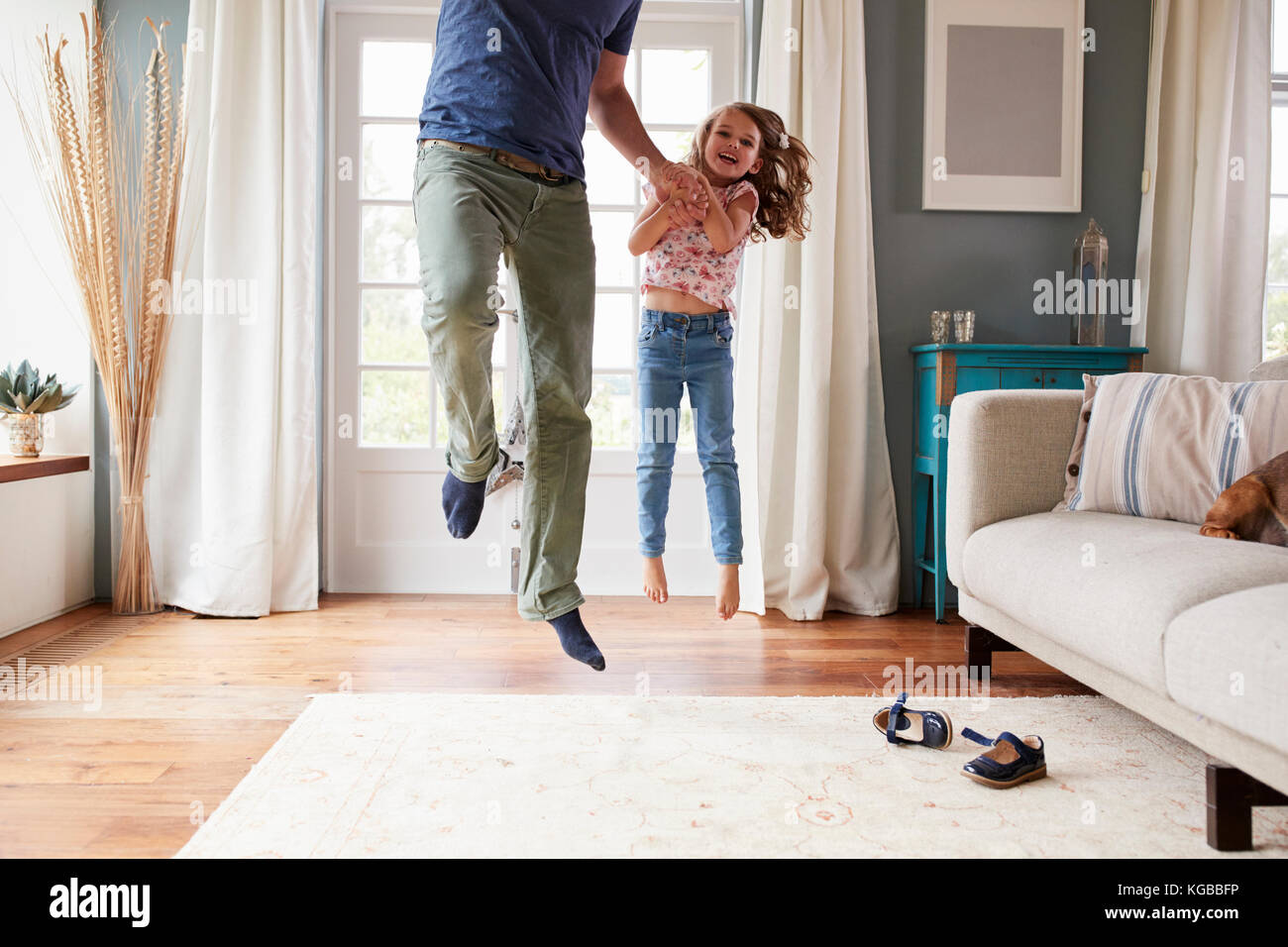 Girl and dad jumping in the air at home holding hands Stock Photo