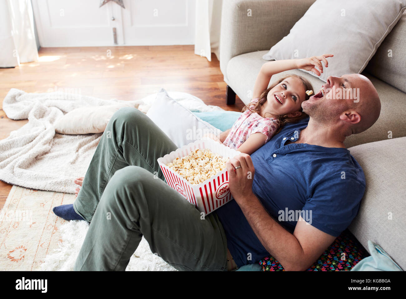 Girl feeding dad popcorn while watching TV together at home Stock Photo