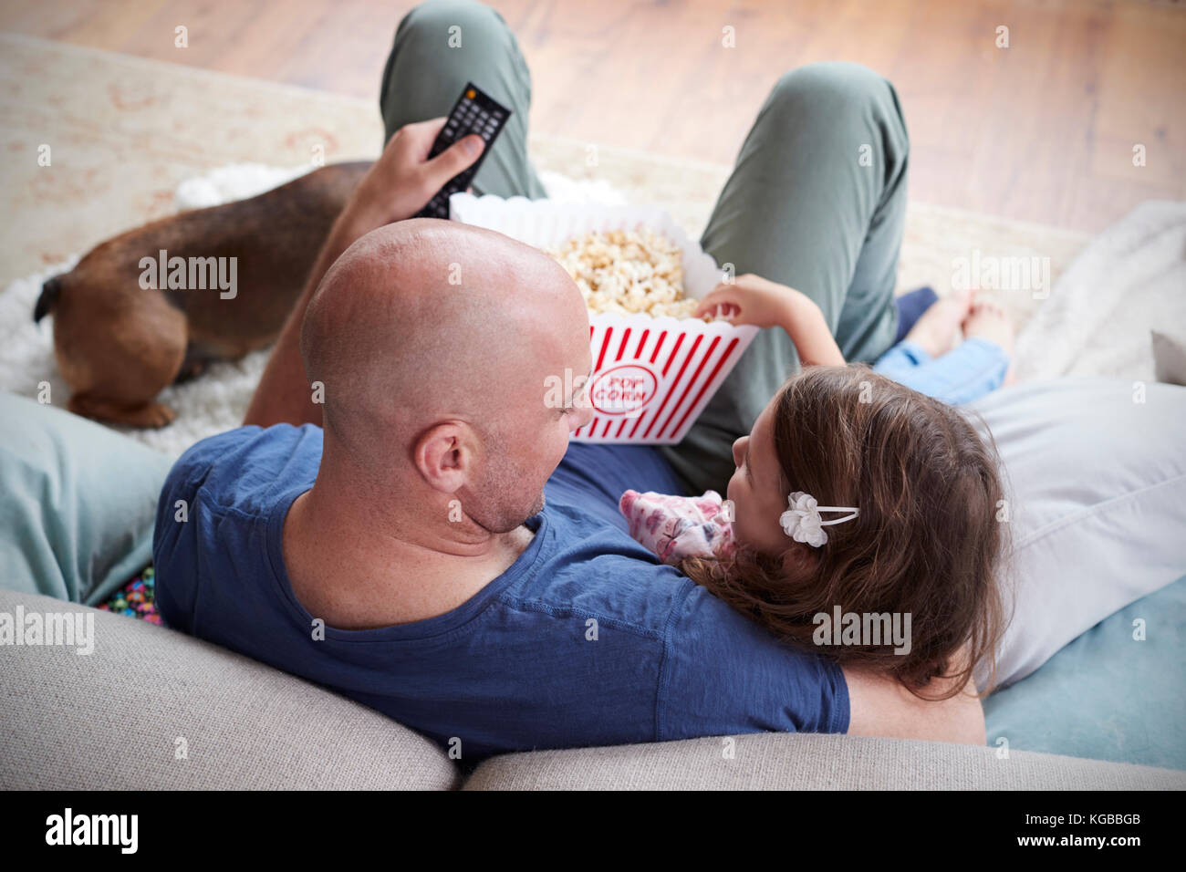 Dad and daughter eating popcorn at home, over shoulder view Stock Photo