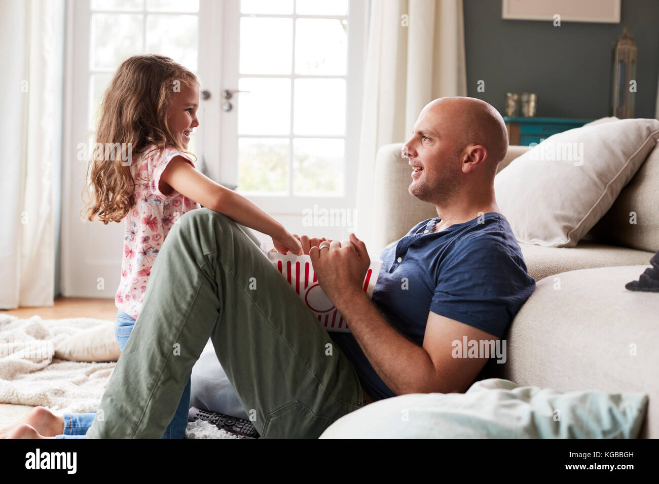 Dad and daughter sitting on the floor at home eating popcorn Stock Photo