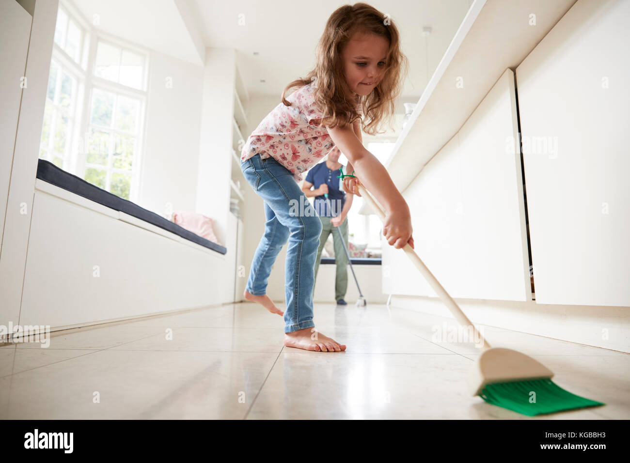 Young girl sweeping kitchen floor, dad in background Stock Photo