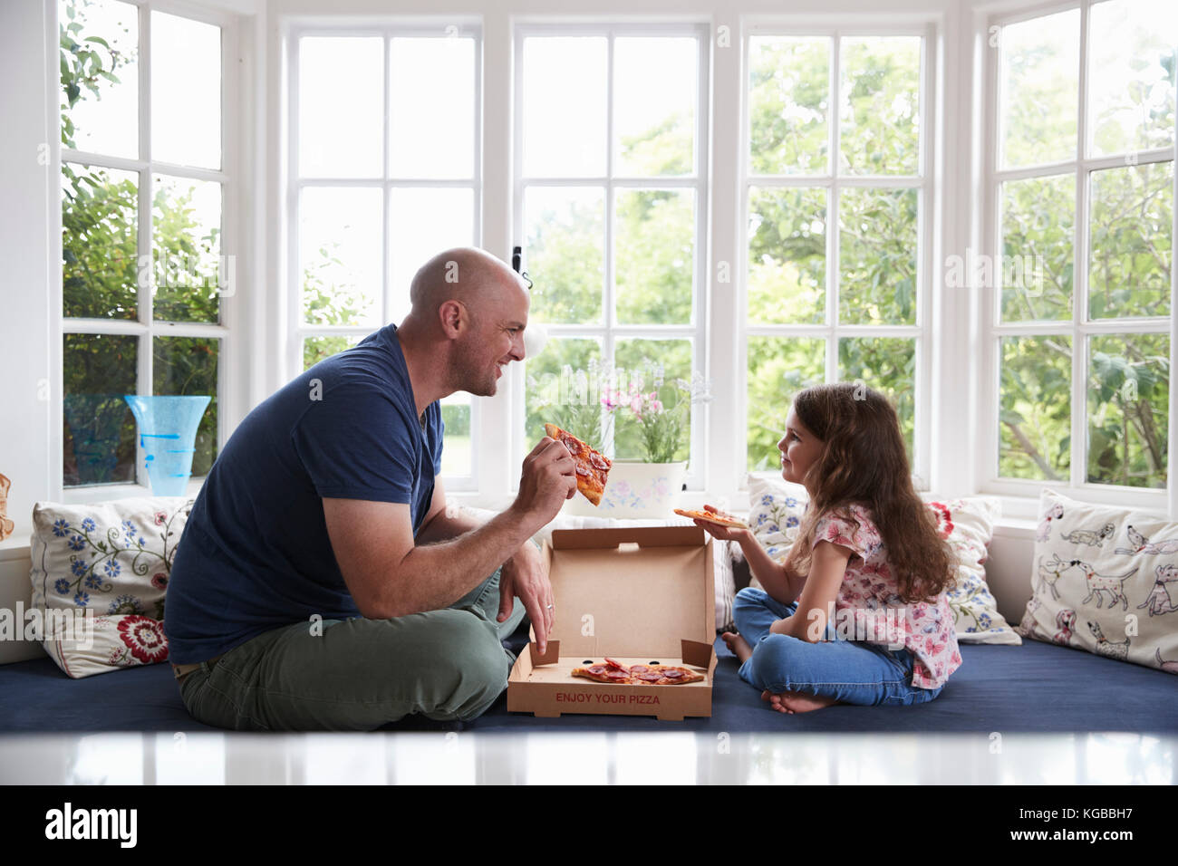 Dad and daughter sit on window seat at home sharing a pizza Stock Photo