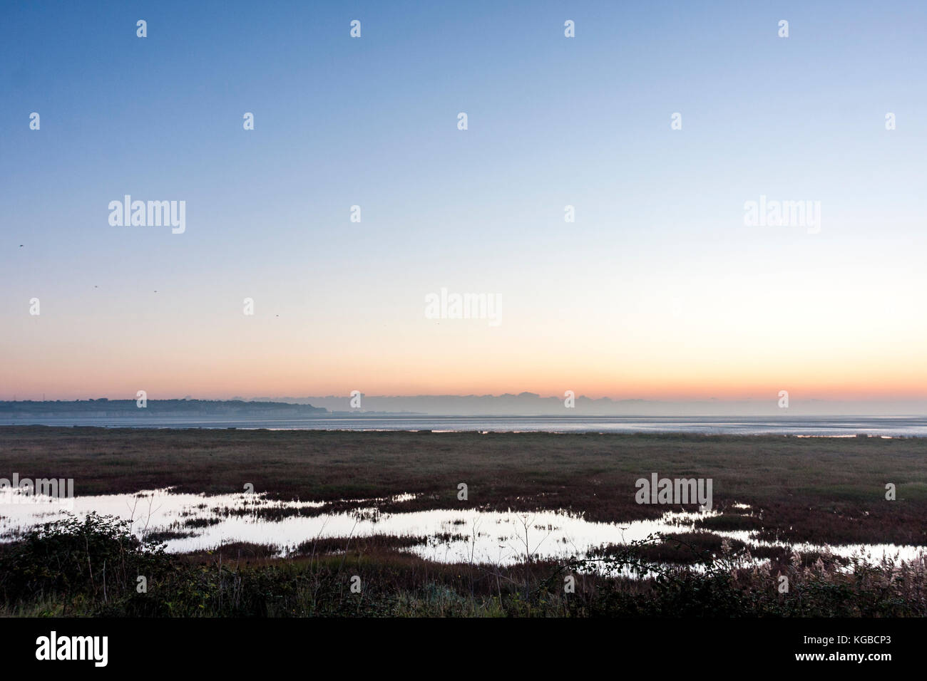 England, Ramsgate, Pegwell Bay. Day break and dawn sky over the English channel with the saltwater marsh in foreground. Band of orange sky on horizon turning to blue. Stock Photo