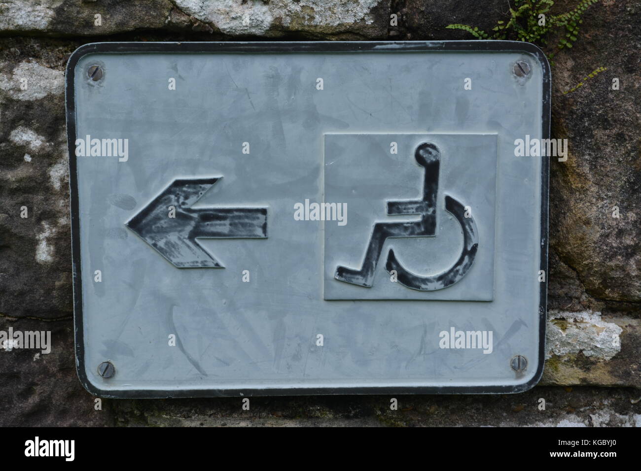 Old weathered black and white rectangular sign screwed to oldstone wall showing directions for wheelchair disabled visitors to ancient ruins buildings Stock Photo