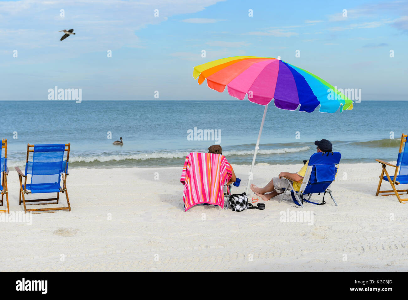 elderly couple sitting on sun loungers with a colorful beach umbrella on silver sand  vacation concept Stock Photo