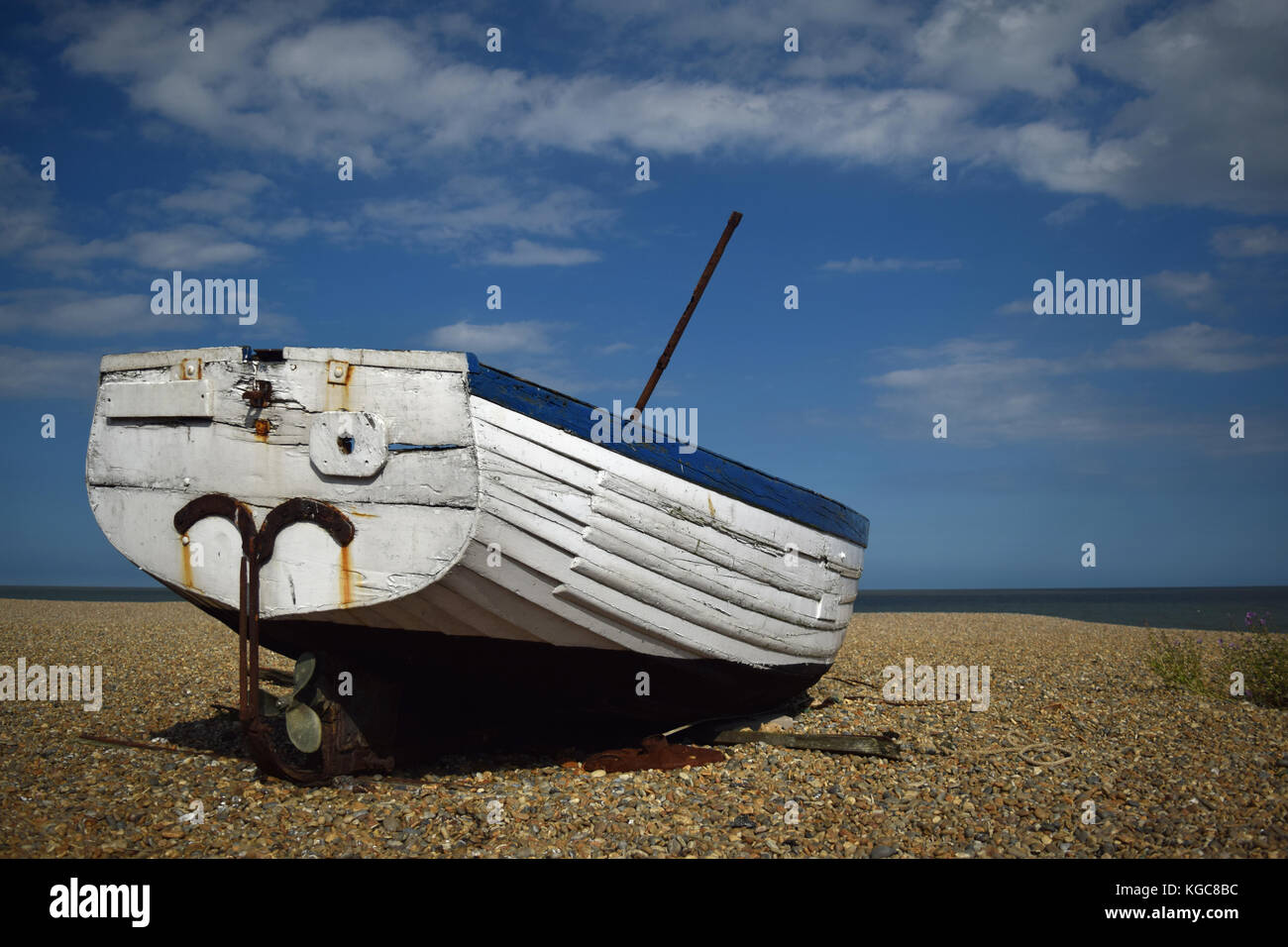 Old blue and white fishing boat abandoned on a pebble beach with a blue ...