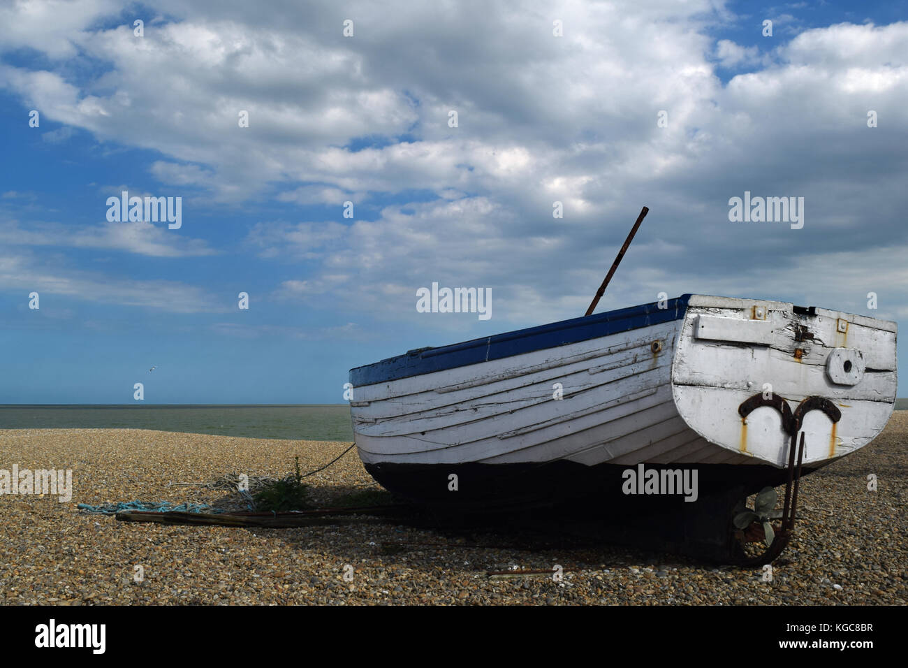 Old blue and white fishing boat abandoned on a pebble beach with a blue ...