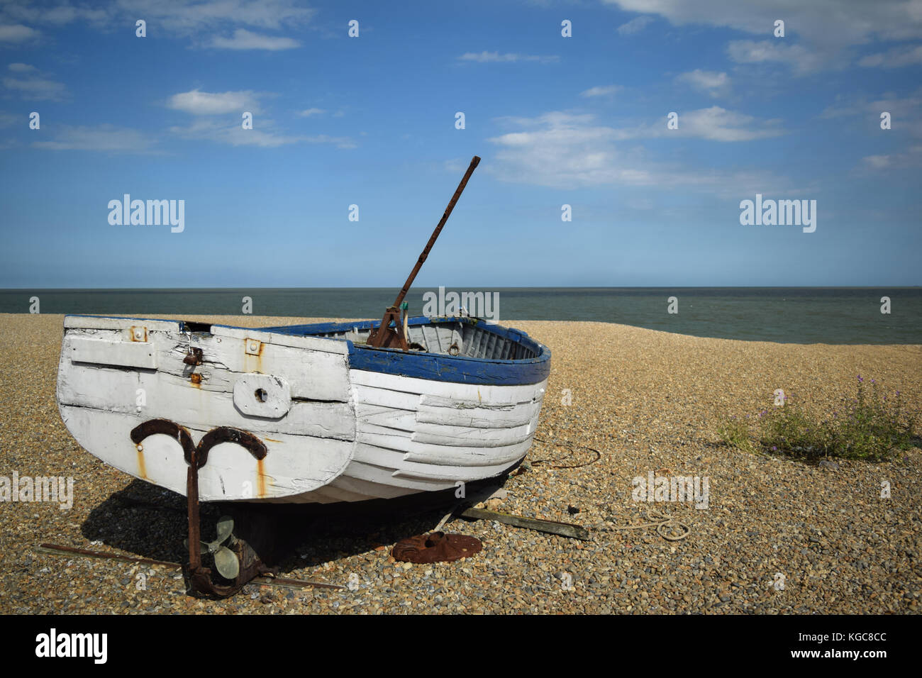 Old blue and white fishing boat abandoned on a pebble beach with a blue ...