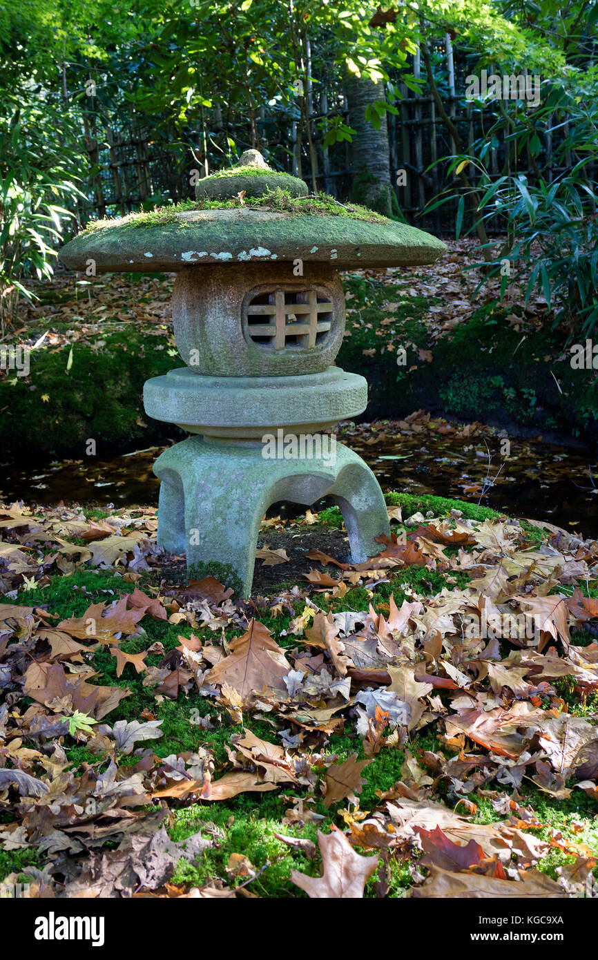 Traditional stone Japanese lantern in autumn in the garden with fallen oak leaves Stock Photo