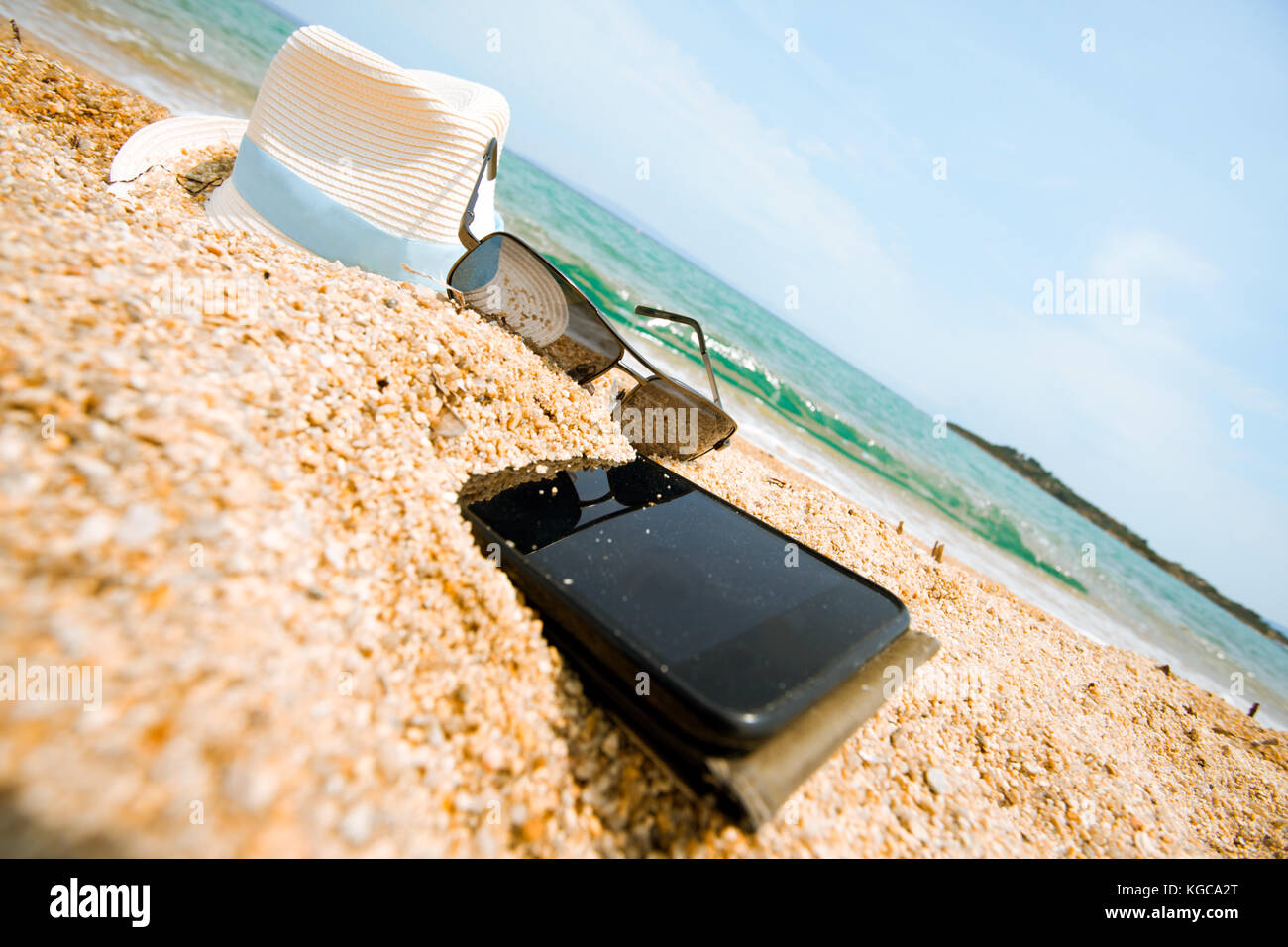 Thrown, half buried in the sand of an ocean or sea shore sand smartphone. Nobody, blue sky with some clouds above. Stock Photo
